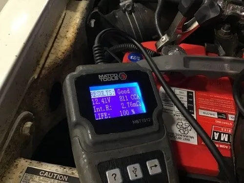A car battery tester displays results of 12.41V, 811 CCA, and 100% life next to a red battery—perfect for routine battery checks in San Antonio auto repair shops.