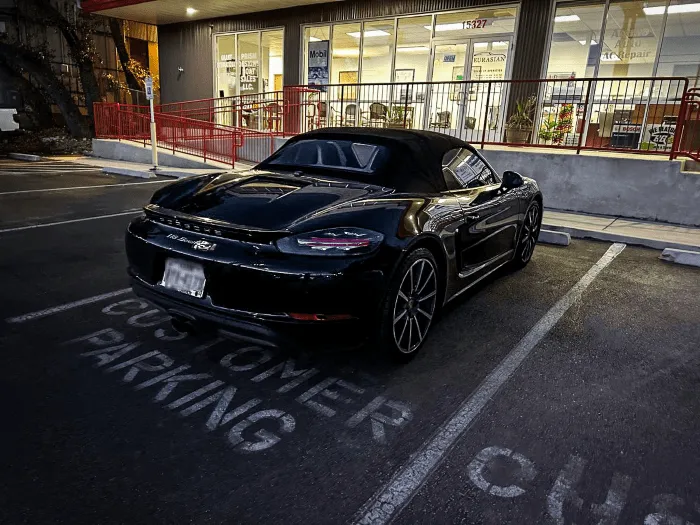 A black convertible sports car is parked in a "Customer Parking" space outside Eurasian Auto Repair, a San Antonio auto repair shop with glass windows at dusk, highlighting the shop's commitment to reliable auto repair and professional auto care.