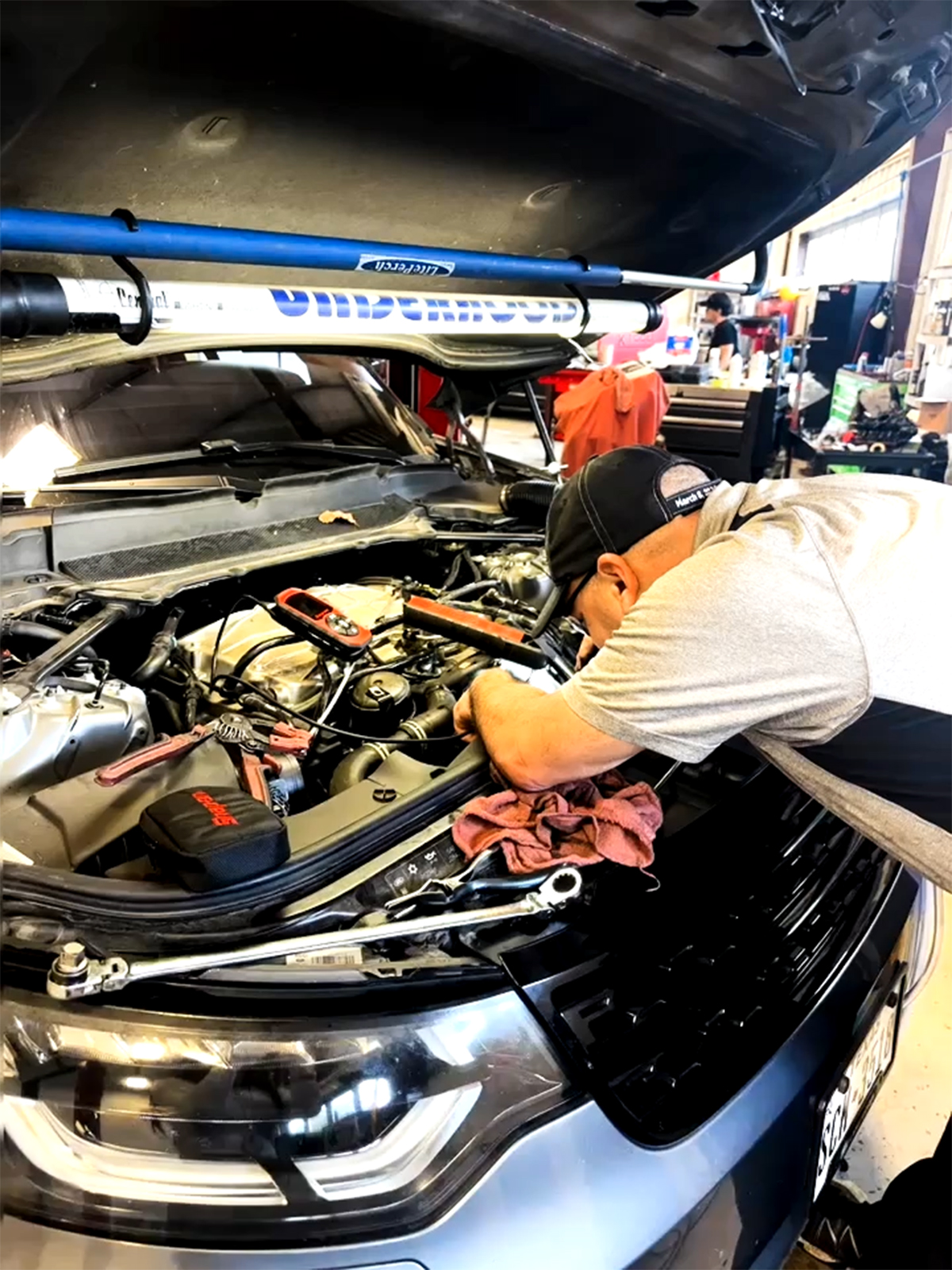 Mechanic working under the hood of a car in a San Antonio auto repair shop with tools and equipment nearby.